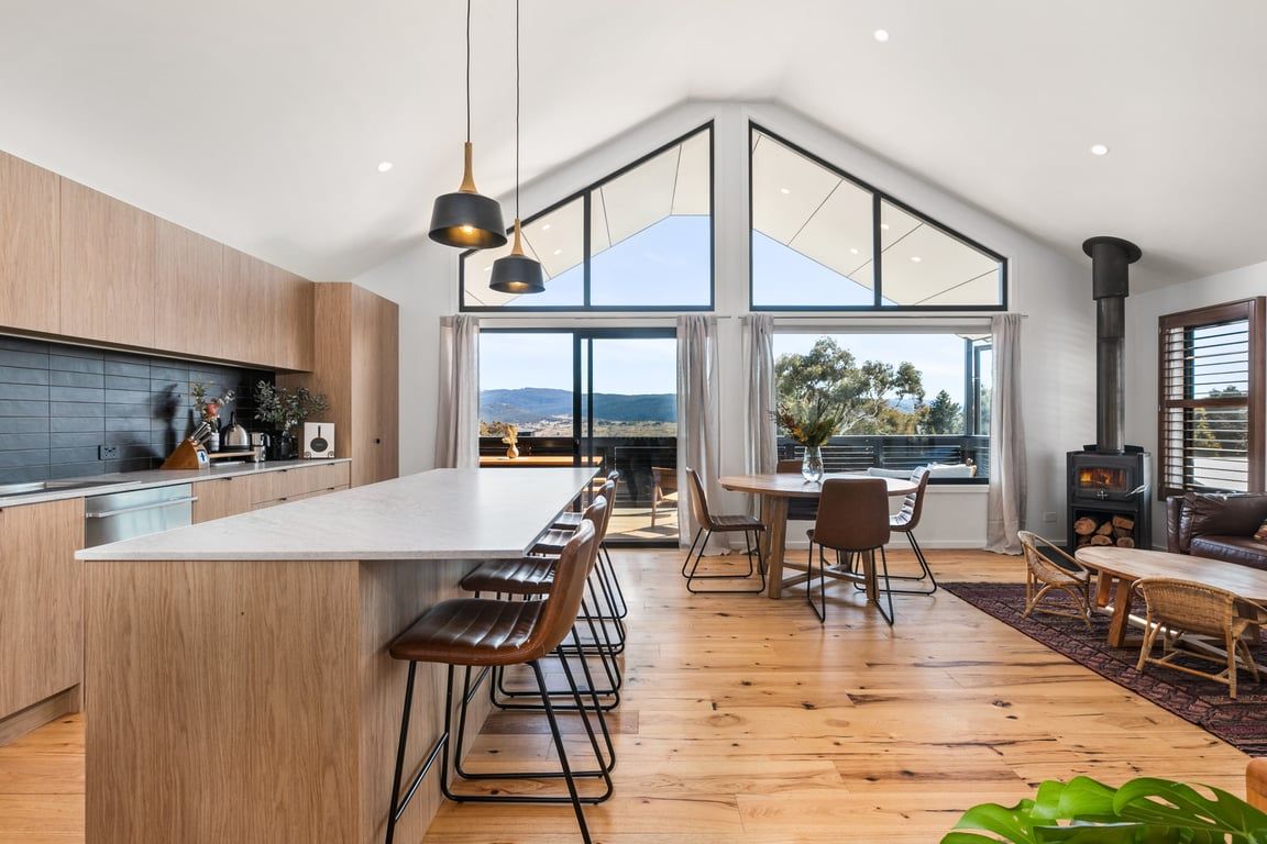 A modern kitchen with a large island, wooden flooring, and a view of the outdoors.