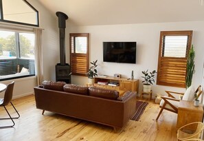 A living room with a sofa, a TV, a fireplace, and wooden blinds. - Heysen Alpine House (Jindabyne)