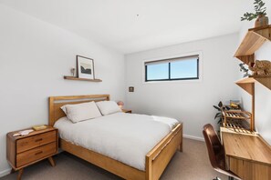 A bedroom with a wooden bed, a nightstand, a desk with a chair, a window, and a shelf with decorative items. - Heysen Alpine House (Jindabyne)