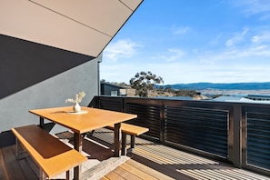 An outdoor seating area with a wooden table and benches, overlooking a scenic landscape. - Heysen Alpine House (Jindabyne)