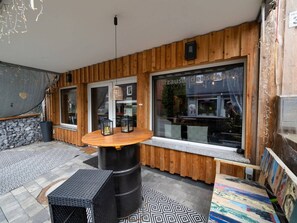 An outdoor seating area with a wooden table and chairs, a stone wall, and a large window with a view of the street. - Resin Passion Braunlage (Braunlage)