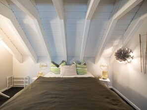 A bedroom with a sloped ceiling, a bed with a dark green bedspread, and decorative pillows. - Resin Passion Braunlage (Braunlage)