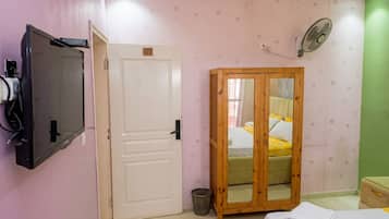 A bedroom with a bed, a wardrobe, a television, and a fan.