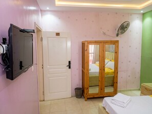 A bedroom with a bed, a wardrobe, a television, and a fan.