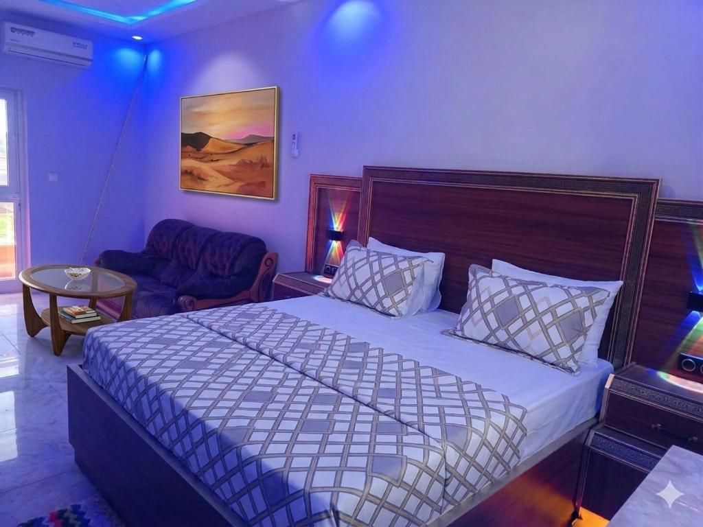 A bedroom with a large bed, a sofa, a small table, and a painting on the wall.