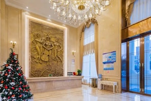 A lobby with a large wall relief, a Christmas tree, and a chandelier. - Vienna Hotel (Chongqing)