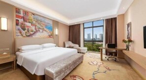 A hotel room with a large bed, a desk, a chair, a TV, and a painting on the wall. - Vienna Hotel (Chongqing)