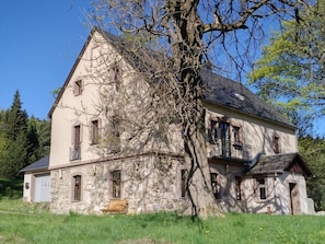 A two-story stone house with a large tree in front, a bench, and a clear blue sky. - Country House Sorgenfrey (Altenberg)