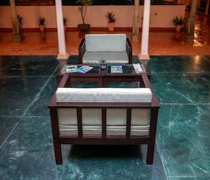 Un sof á de madera oscura con un cojín, un sillón a juego y una mesita con revistas y una planta.