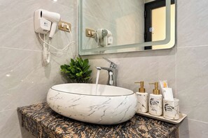A bathroom with a marble sink, a hairdryer, a mirror, and toiletries on a shelf. - Trang An Lucky Homestay (Tây Hoa Lư)