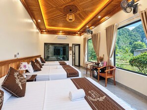 Een hotelkamer met twee bedden, een zithoek met een stoel, een groot raam met gordijnen en uitzicht op groen.