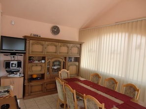 A dining area with a table set for six, flanked by wooden chairs with cushioned seats. A television is mounted on the wall above the table. - Holiday Home in Vir With Swimming Pool (Vir)