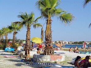 A beach with palm trees, people sunbathing, and a clear sky. - Holiday Home in Vir With Swimming Pool (Vir)