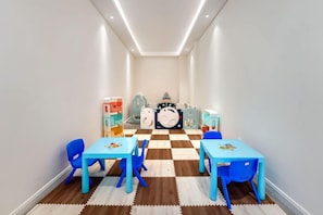 Una sala de jocs infantil amb dues taules i cadires blaves, un terra de pissos i una fila d'unitats d'emmagatzematge de colors.