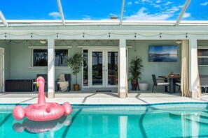 Ein Swimmingpool mit einem rosa Flamingo-Luftballon, einer überdachten Terrasse und einem Esstisch mit Stühlen.