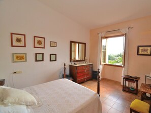 Ein Schlafzimmer mit Bett, Kommode, Spiegel, Fenster mit Vorhängen und Bildern an der Wand.