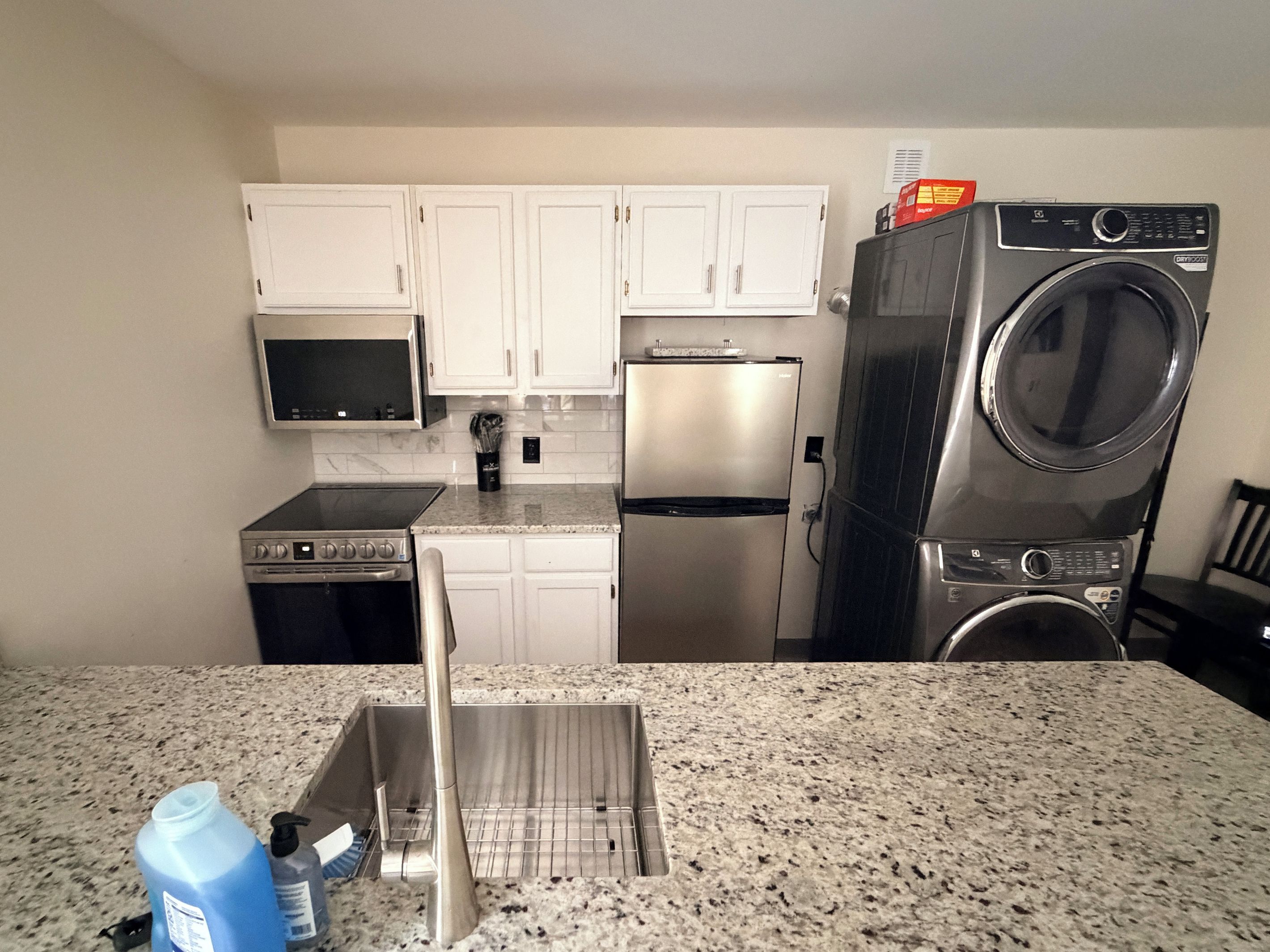 A kitchen with white cabinets, a stainless steel refrigerator, a microwave, a stove, and a washing machine.