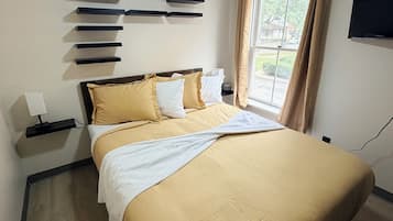 A hotel room with a bed, a ceiling fan, a window with curtains, and a wall-mounted TV.