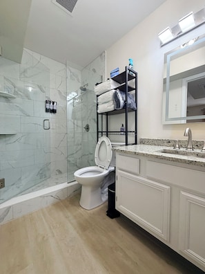 A bathroom with a toilet, a shower, and a vanity with a mirror.