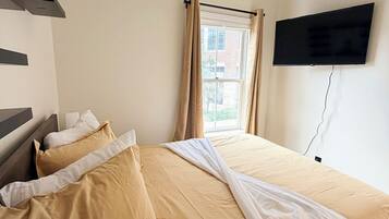 A bedroom with a bed, a ceiling fan, a window with curtains, and a mounted television.