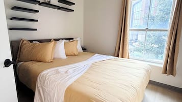 Un dormitorio con cama, ventilador de techo, ventana con cortinas y estante de pared con una figurita.