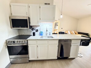 A compact kitchen with white cabinets, a microwave, an oven, and a dishwasher.