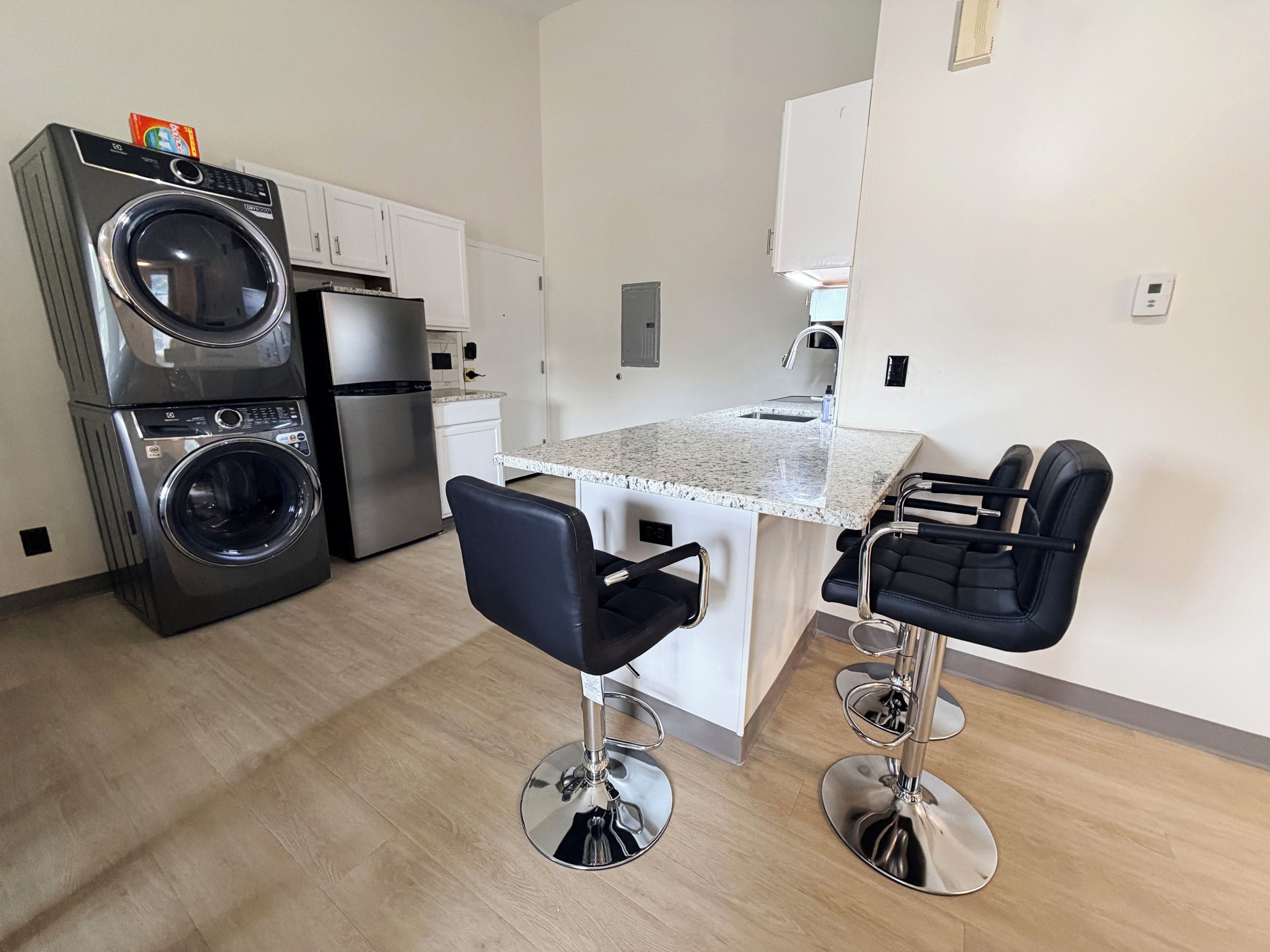 Unit 6 Kitchen showing fridge, in unit washer and dryer, and bookshelf with Keurig, k-cups, toaster, and tea.