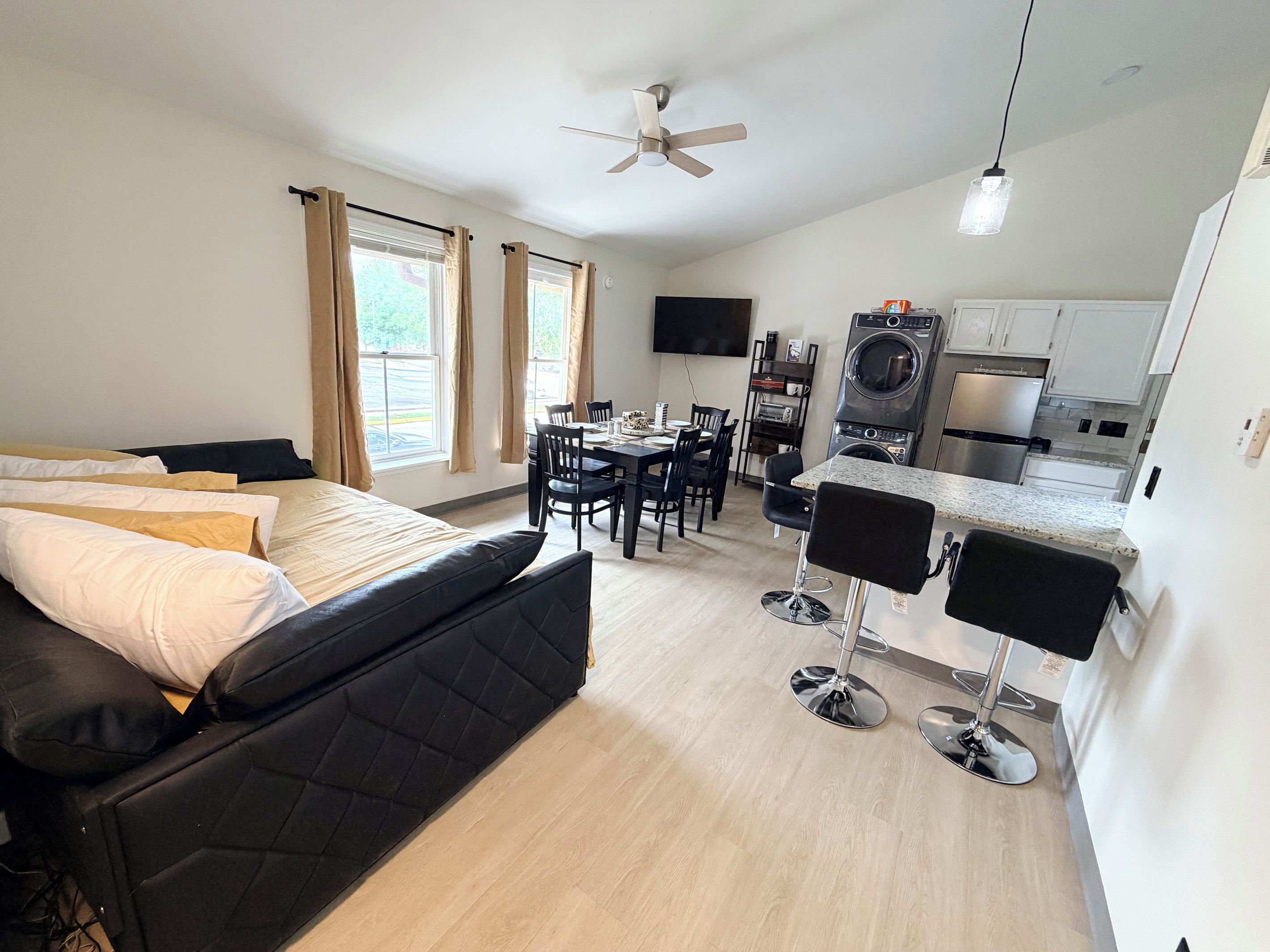A modern hotel room with a bed, a dining area, and a kitchenette.