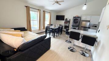 A modern hotel room with a bed, a dining area, and a kitchenette.