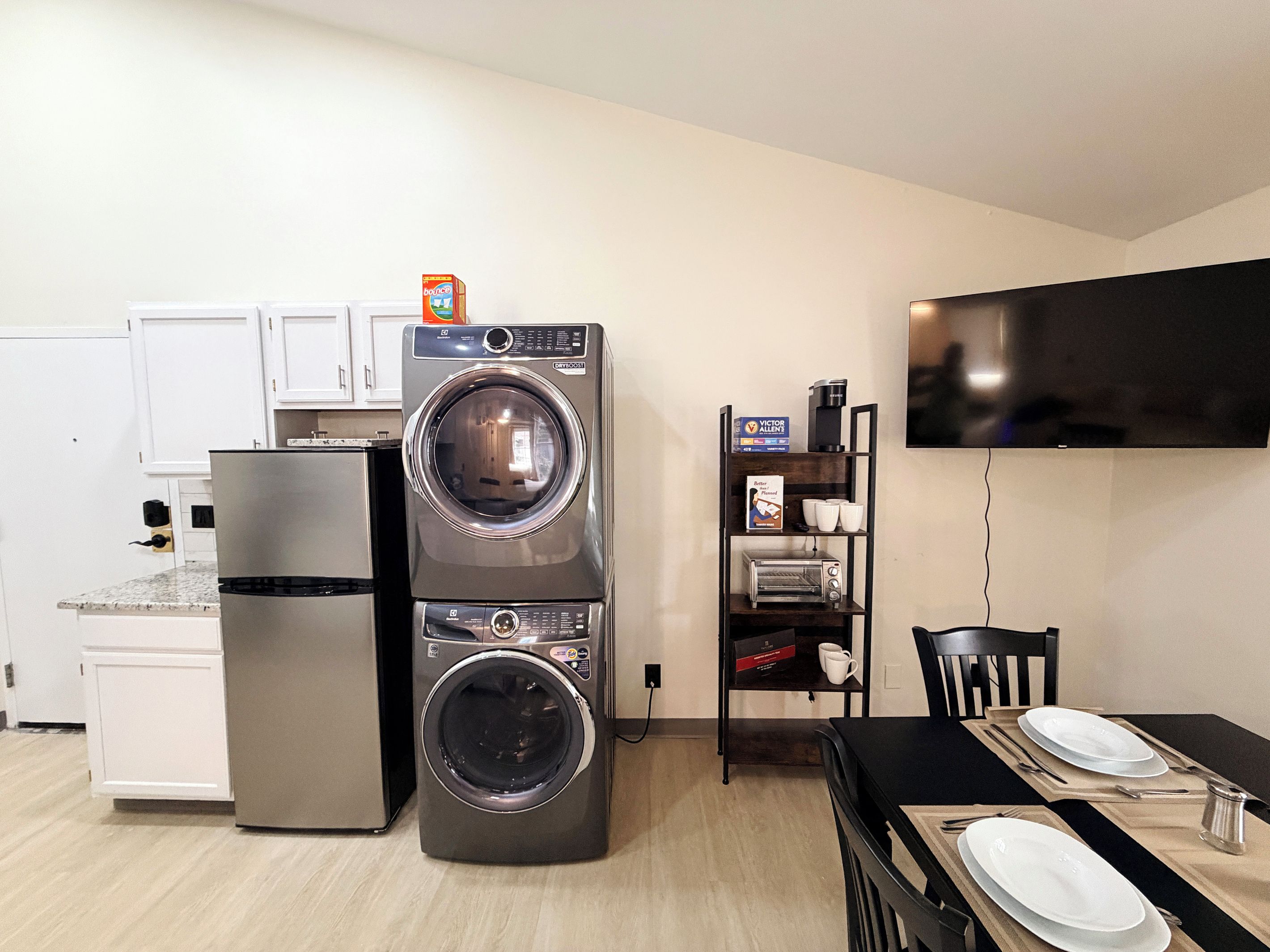 A compact kitchen with a washing machine, a refrigerator, a microwave, and a dining area with a table set for two.