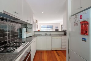 Una cocina moderna con gabinetes blancos, estufa a gas, lavavajillas y refrigerador.