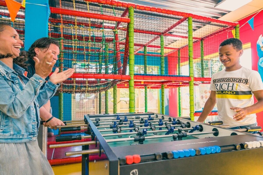 Una mesa de fútbol de mesa en un área de juegos interior de colores brillantes con estructuras de escalada con red.