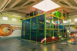 A play structure with netted sides and colorful elements, set in a room with a high ceiling and a mural on the wall. - Holiday home in Mol with kettle (Mol)