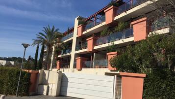 A multi-story residential building with balconies, a gated entrance, and surrounding greenery.