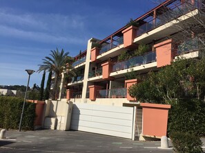 Un edifici residencial de diversos pisos amb balcons, una entrada tancada i vegetació als voltants.