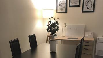 A dining table with chairs, a plant, and a lamp. There are framed pictures on the wall.
