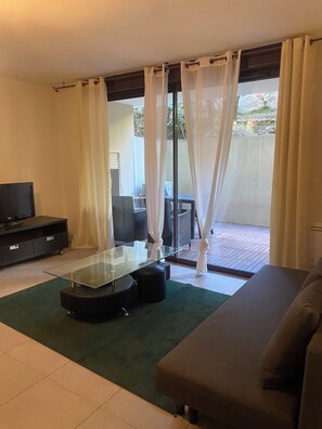 A living room with a glass-top coffee table, a sofa, a TV on a cabinet, and a sliding glass door leading to an outdoor area. - Vrbo Property (Montpellier)