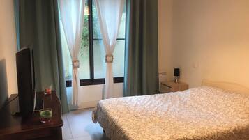 A hotel room with a bed, a bedside table, a lamp, and a window with curtains.