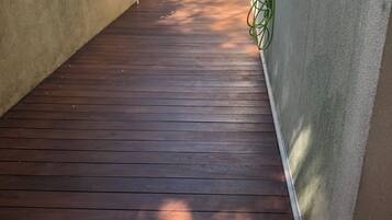 Una terraza de madera estrecha con una silla a lo lejos, rodeada de muros cubiertos de vegetación.