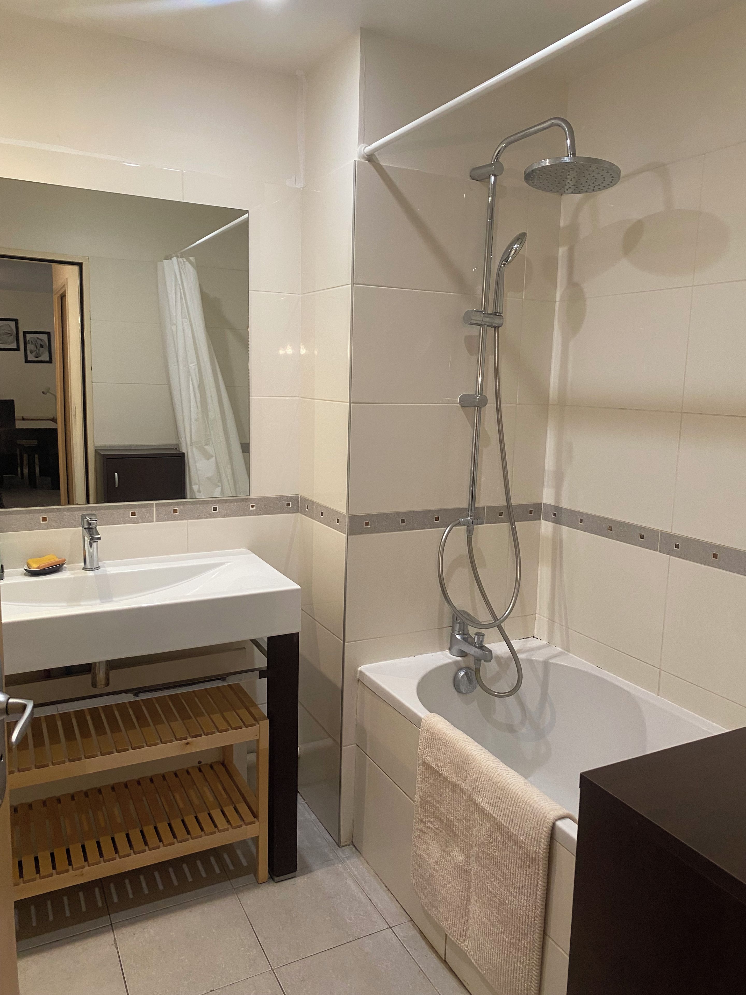 A bathroom with a sink, mirror, shower, and a towel rack.