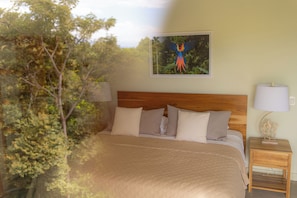 Ein Schlafzimmer mit Holz-Kopfteil, einem Bett mit beigefarbener Bettwäsche, einem Nachttisch mit Lampe und einem gerahmten Vogelbild an der Wand.