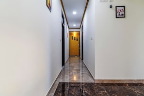 Un passadís amb sòl de marbre, una porta de fusta al final i quadres als murs.
