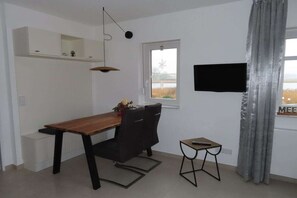 A dining area with a wooden table, black chairs, a small side table, a television mounted on the wall, and a window with a view of the outdoors. - in the Seedorf holiday park (Neuensien- Sellin)