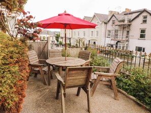 An outdoor patio with a wooden table and chairs, a red umbrella, and a view of residential buildings. - Tudno Lodge (Llandudno)