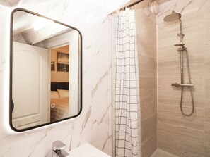 Ein Badezimmer mit Marmorwand, einer Dusche inklusive Handbrause und einem Spiegel mit schwarzem Rahmen.