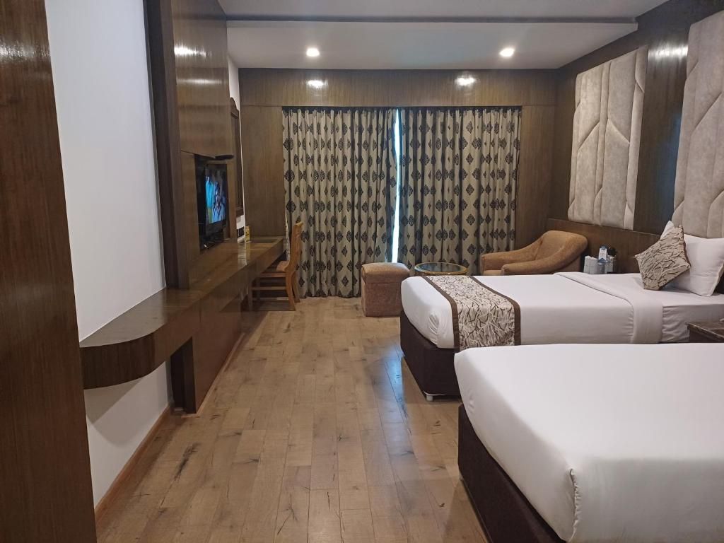 Ein Hotelzimmer mit Holzboden, einem Fernseher, zwei Betten, einer Couch und einem kleinen Tisch.