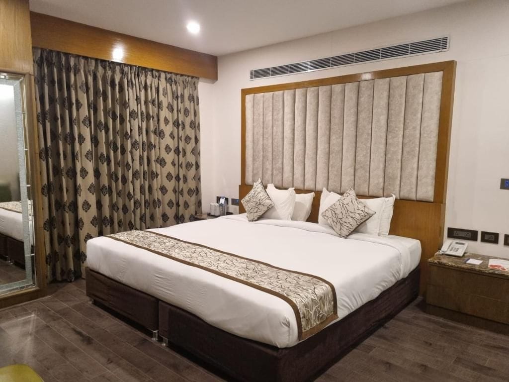 Habitación de hotel con una cama grande, cabecera, mesita de noche y espejo.