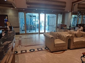 A lobby with a reception desk, a seating area with two sofas, and a glass door entrance. - Benzz Park -Chennai (Chennai)