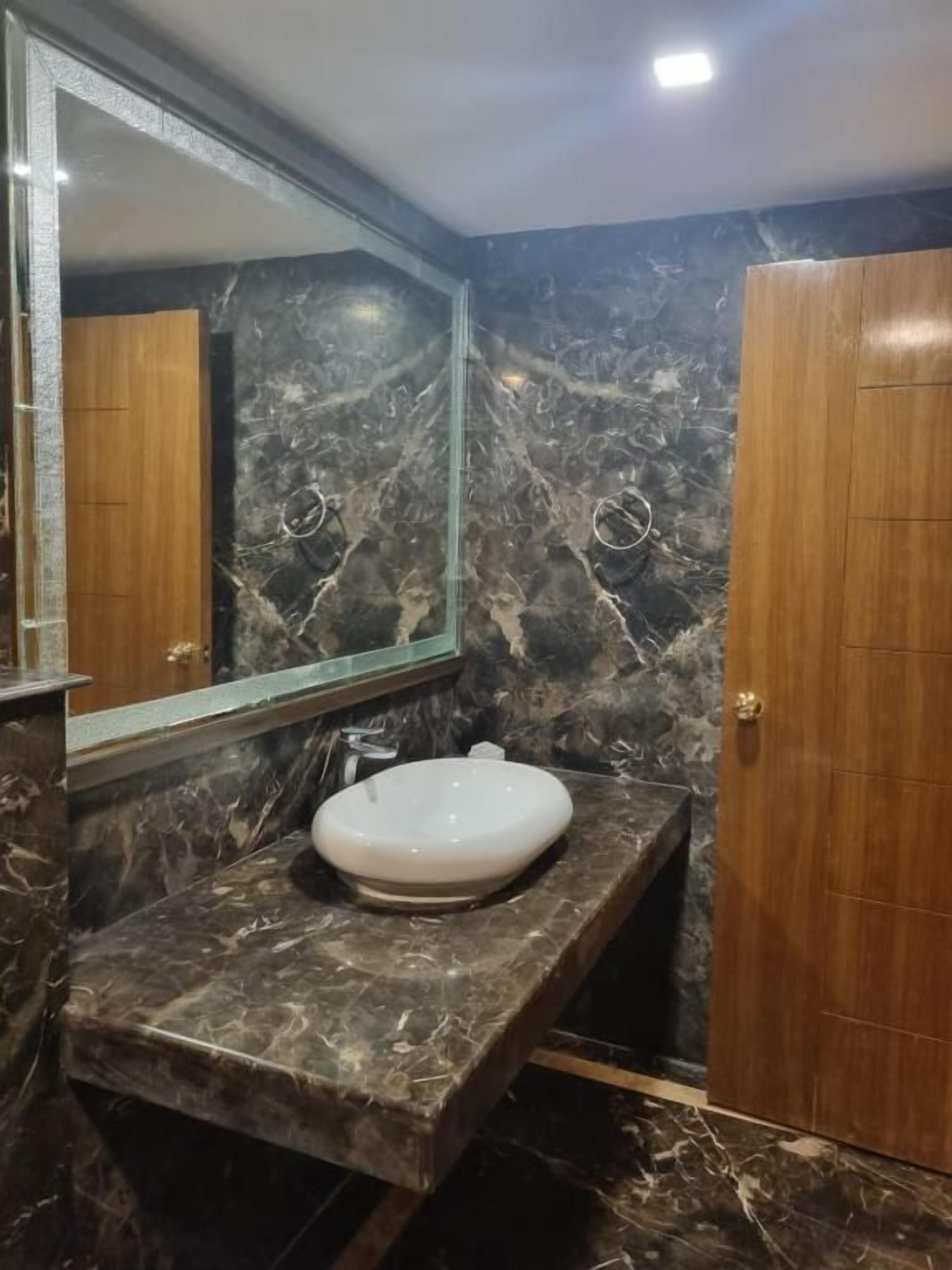Un baño con encimera de mármol, un lavamanos blanco y una puerta de madera.
