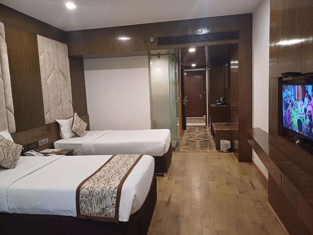 A hotel room with two beds, a television, and a hallway leading to a bathroom.